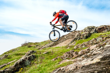 Fototapeta na wymiar Cyclist in Red Jacket Riding Mountain Bike Down Rocky Hill. Extreme Sport and Adventure Concept.