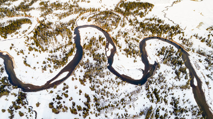 Winding river leads through a forest in winter with snow on the ground