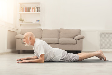 Senior man training yoga in cobra pose indoors