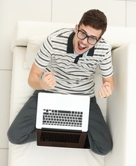 view from the top. jubilant young man with laptop sitting on the couch