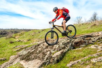 Fototapeta premium Cyclist in Red Jacket Riding Mountain Bike Down Rocky Hill. Extreme Sport and Adventure Concept.