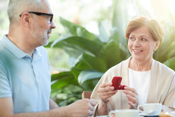 Mature woman holding red velvet box with diamond ring and saying thanks to her husband while spending time together