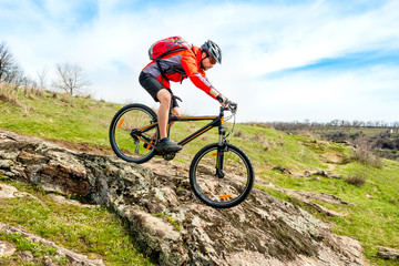 Cyclist in Red Jacket Riding Mountain Bike Down Rocky Hill. Extreme Sport and Adventure Concept.