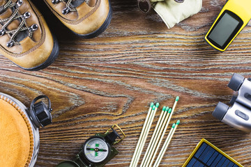 Hiking or travel equipment with boots, compass, binoculars, matches on wooden background. Active lifestyle concept