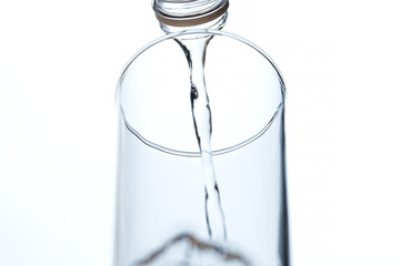 Perk view and close up. Water poured from a bottle into a glass empty. On white background.