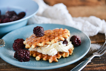 Round waffles with fresh blackberries and whipped cream, on natural wooden background in rustic style