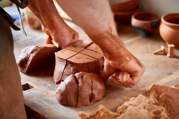 Adult male potter master modeling the clay plate on potter's wheel. Top view, closeup, hands only.