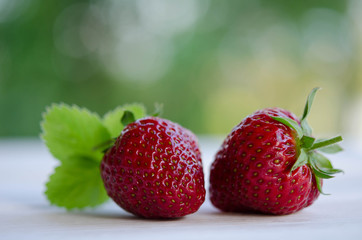 two strawberries  with leaves on wooden table/ outdoor photo