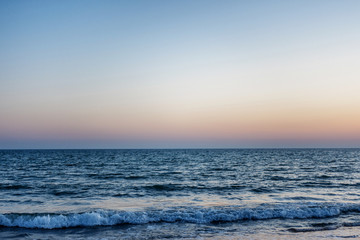 blue sea at sunset. the waves are to the shore. the sun over the horizon