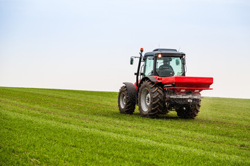 Farmer in tractor fertilizing wheat field at spring with npk