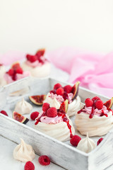 Fototapeta na wymiar Delicious mini Pavlova meringue cake decorated with fresh raspberry, figs and berry sauce