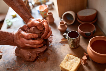 Adult male potter master modeling the clay plate on potter's wheel. Top view, closeup, hands only.