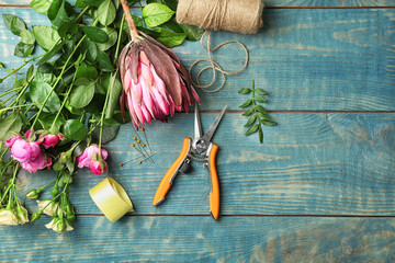 Florist equipment with flowers on wooden background, top view