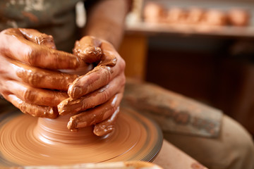 Adult male potter master modeling the clay plate on potter's wheel. Top view, closeup, hands only.
