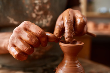 Adult male potter master modeling the clay plate on potter's wheel. Top view, closeup, hands only.