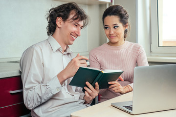 a guy with a diary in his hand laughs in the kitchen with his girlfriend in the kitchen.