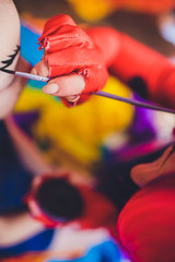 Drawing a face painting on a girl's face. Painter's brushes and hands