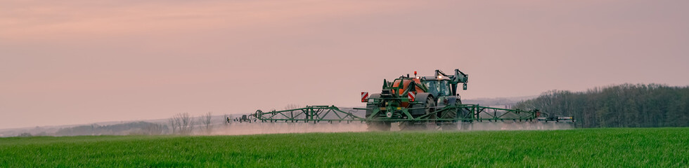 Fototapeta premium Ackerbau - Landwirt bei Pflanzenschutzmaßnahmen im Getreide am Abend, Banner