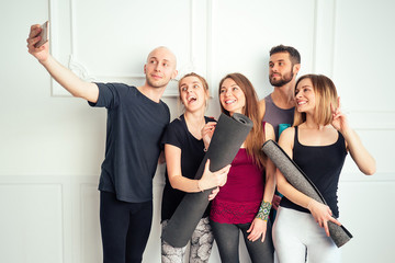 Fototapeta premium a happy group of people from man and woman practicing yoga in the studio and making selfies on the phone. groups of meditation and support in the yoga class. men and women have fun