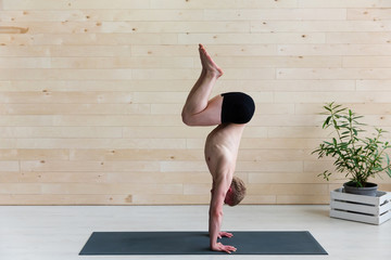 Sporty man practices yoga handstand asana Adho Mukha Vrikshasana at the yoga studio. Balance exercise