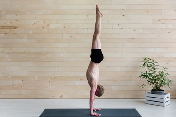 Sporty man practices yoga handstand asana Adho Mukha Vrikshasana at the yoga studio. Balance...