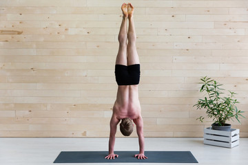 Sporty man practices yoga handstand asana Adho Mukha Vrikshasana at the yoga studio. Balance...