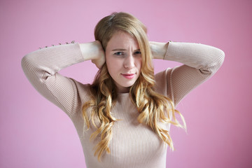 Horizontal shot of stressed attractive young woman frowning, covering ears with both hands, can't...