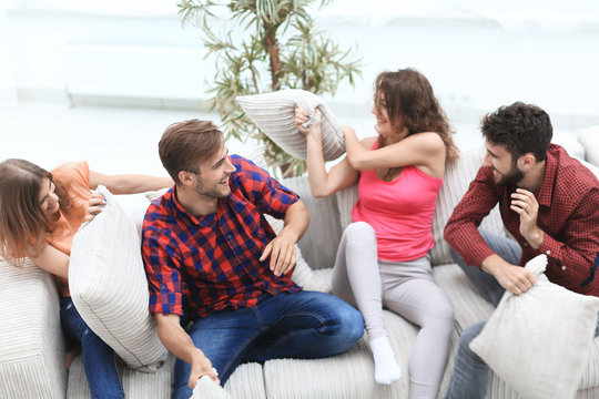 group of friends playing pillow fight, sitting on the couch