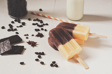 Two-colored ice cream on a stick, beige brown on a white table. Coffee vanilla ice cream, toned photo.
