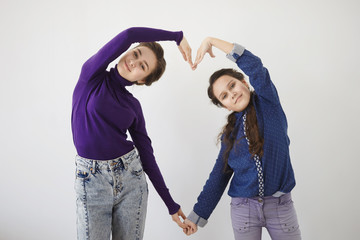 People, family, love and happiness concept. Portrait of cheerful young mother and her daughter posing in studio together, holding hands, forming heart shape, looking and smiling broadly at camera