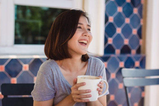 Portrait of happy young asian business woman with mug in hands drinking coffee in the morning at cafe. Asian women express emotion relax at the cafe or coffee shop. Woman food and drink cafe concept.