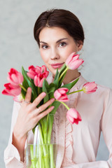 Beautiful young woman with spring tulips flowers bouquet. Happy girl smiling holds flowers, pink tulip. Spring portrait of pretty female