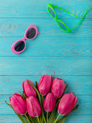 Women's accessories - sunglasses and bouquet of pink tulips on a wooden background.