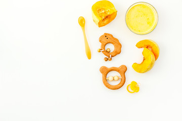 Healthy food for little baby. Puree with pumpkin near pacifier and toys on white background top...