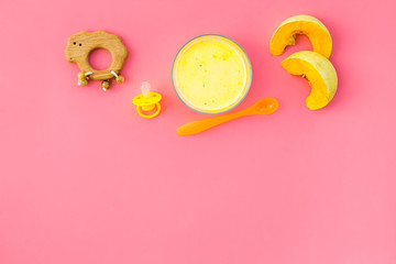 Healthy food for little baby. Puree with pumpkin near pacifier and toys on pink background top view copy space