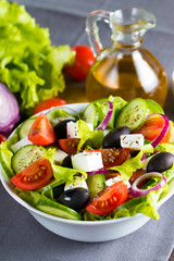Fresh Greek salad made of cherry tomato, ruccola, arugula, feta, olives, cucumbers, onion and spices. Caesar salad in a white bowl on wooden background. Healthy organic diet food concept.