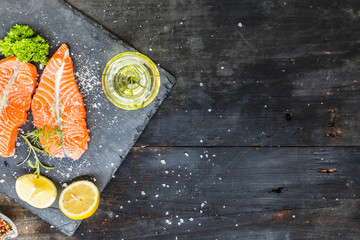 Salmon, Red fish medallions on slate tray with lemon and spices on old black smoked rustic wooden...