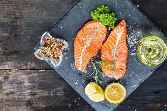 Salmon, Red fish medallions on slate tray with lemon and spices on old black smoked rustic wooden background, top view, copy space