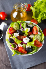 Fresh Greek salad made of cherry tomato, ruccola, arugula, feta, olives, cucumbers, onion and spices. Caesar salad in a white bowl on wooden background. Healthy organic diet food concept.