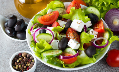 Fresh Greek salad made of cherry tomato, ruccola, arugula, feta, olives, cucumbers, onion and spices. Caesar salad in a white bowl on wooden background. Healthy organic diet food concept.
