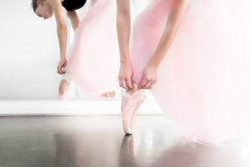Young ballerina in pink airy tutu skirt tightening her pink atlas pointe shoes