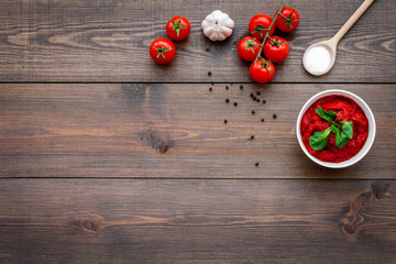 Ingredients for tomato sauce. Cherry tomatoes, garlic, green basil, black pepper, salt in spoon on dark wooden background top view copy space