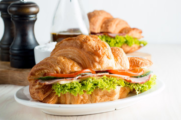 Fresh croissant or sandwich with salad, ham, jamon, prosciutto, salami, cheese, chicken, tomatoes on wooden background. Morning breakfast concept. Healthy and fast food.