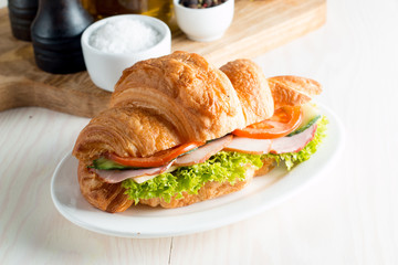 Fresh croissant or sandwich with salad, ham, jamon, prosciutto, salami, cheese, chicken, tomatoes on wooden background. Morning breakfast concept. Healthy and fast food.