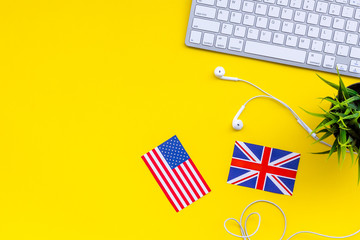 Learn english online. Computer keyboard, headphones, british and american flags on yellow background top view copy space
