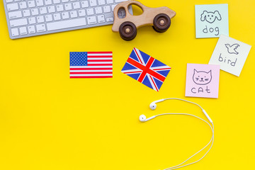 Fototapeta na wymiar Teach english to a child. Funny english. British and american flags, computer keyboard, stickers with vocabulary, toy on yellow background top view copy space