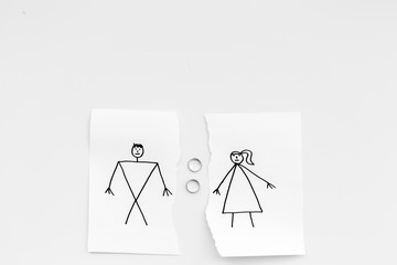 Divorce or falling apart concept. Torn sheet of paper with drawn man and woman, wedding rings between parts on white background top view copy space