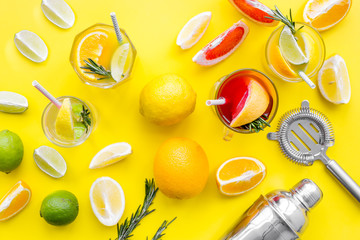 Mix exotic fruit cocktail with alcohol. Shaker and strainer near citrus fruits and glass with cocktail on yellow background top view pattern