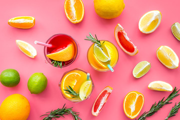 Tropical fruit cocktail with alcohol. Glass with beverage near oranges, grapefruit, lime and rosemary on pink background top view pattern