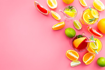 Tropical fruit cocktail with alcohol. Glass with beverage near oranges, grapefruit, lime and rosemary on pink background top view copy space
